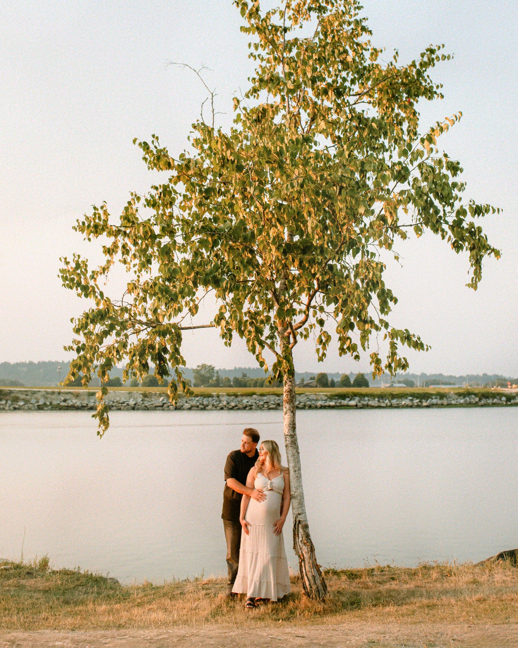 Couple beneath a birch tree at the water’s edge in golden-hour light