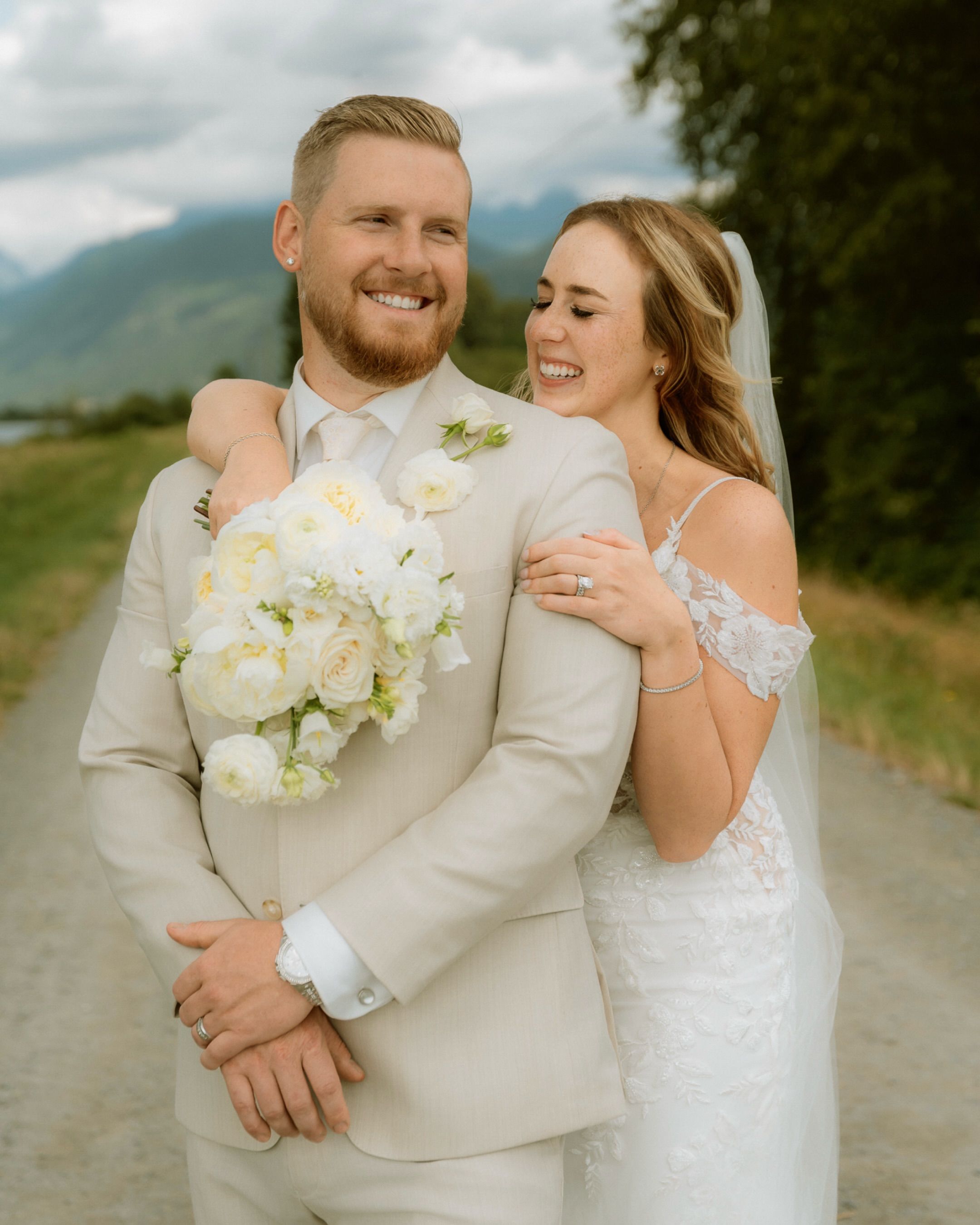 Bride and groom laughing together with a white bouquet on a country road