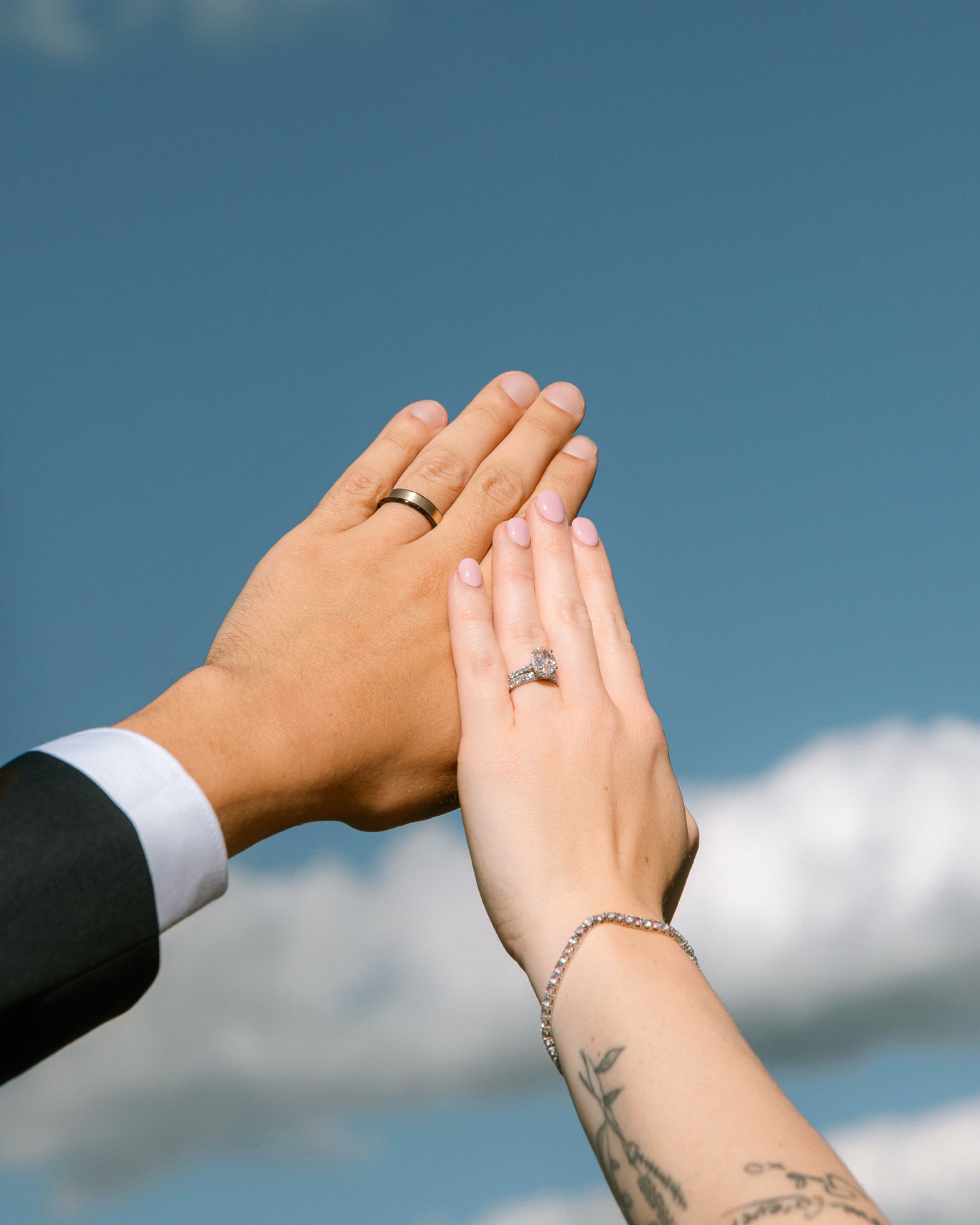 Two hands raised against a blue sky showing their wedding rings