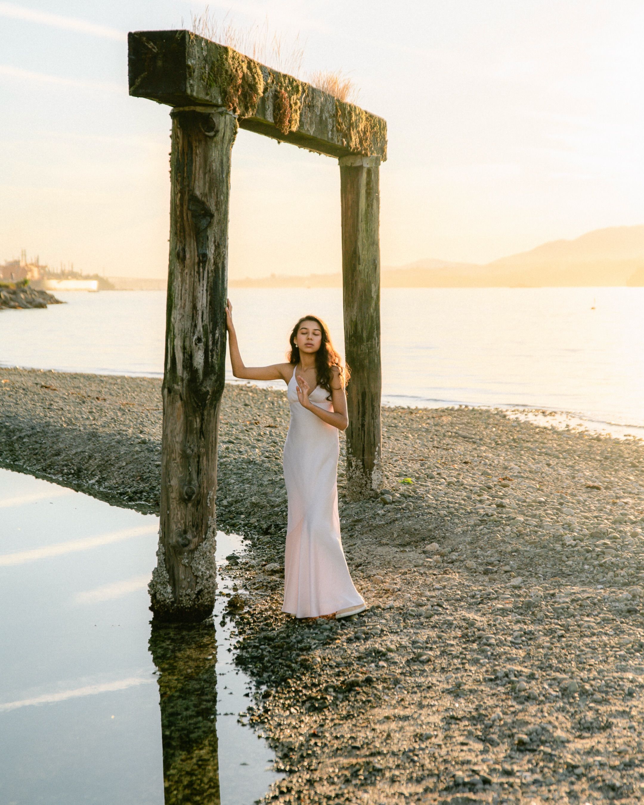 Woman in a pale dress under a weathered pier at sunset