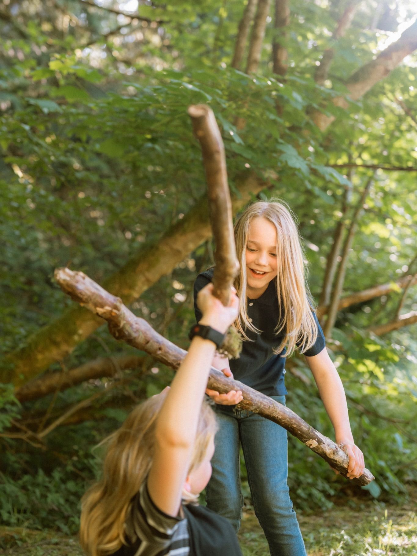 Two children playing with a long branch in a summer forest