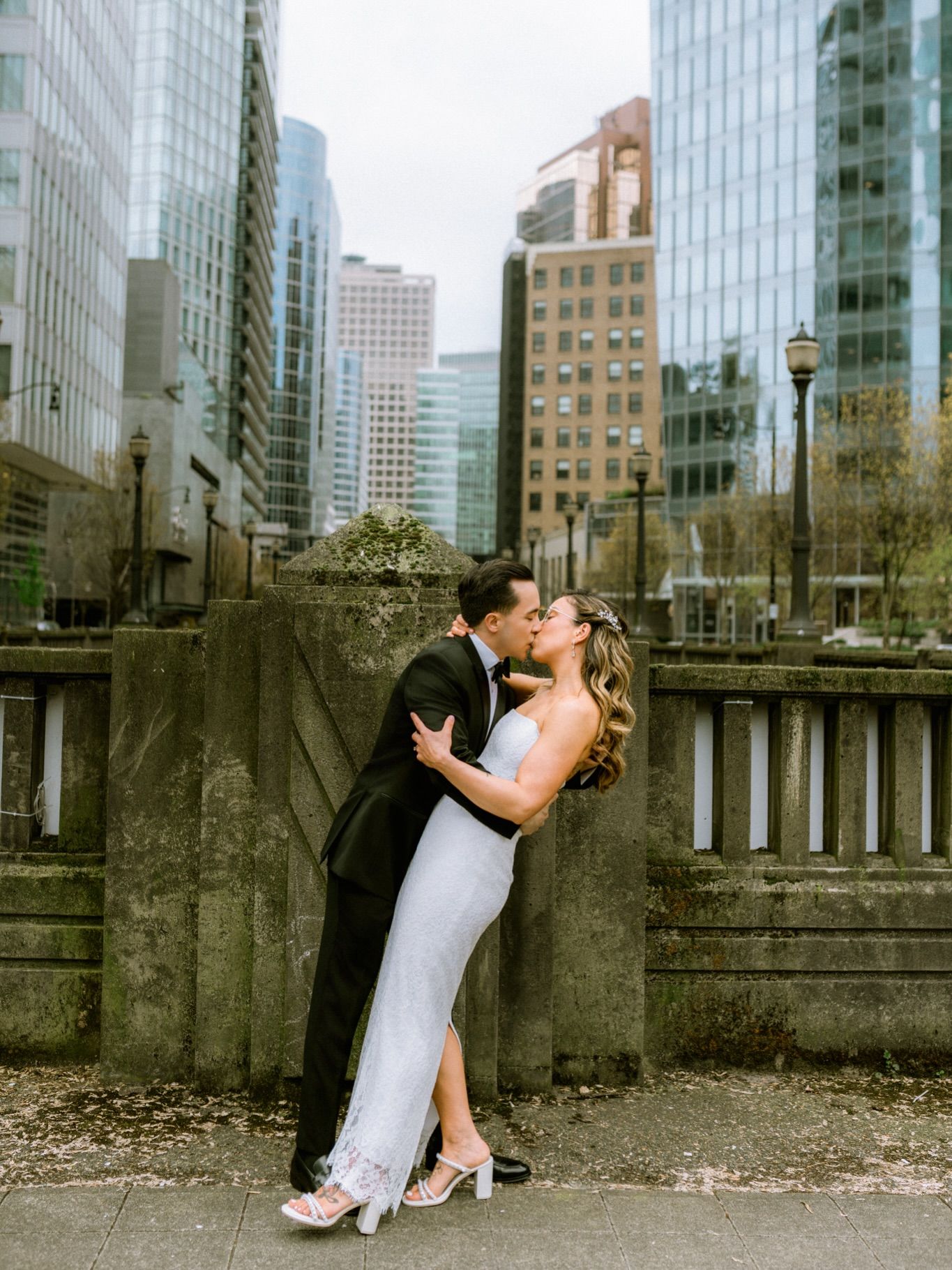 Couple kissing on a city bridge with downtown towers behind them