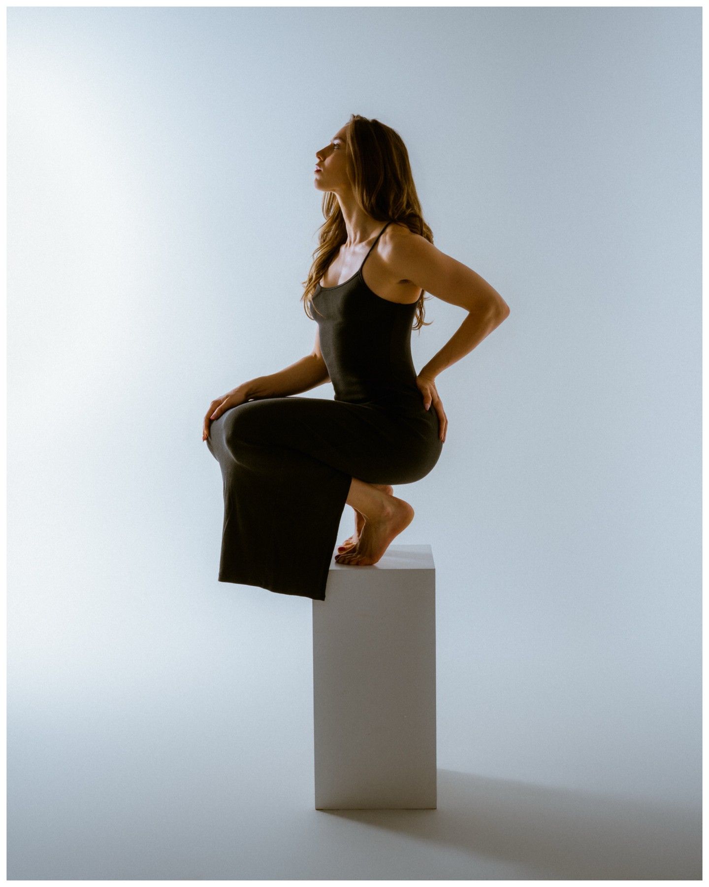 Woman in a black dress posed on a white plinth in a bright studio