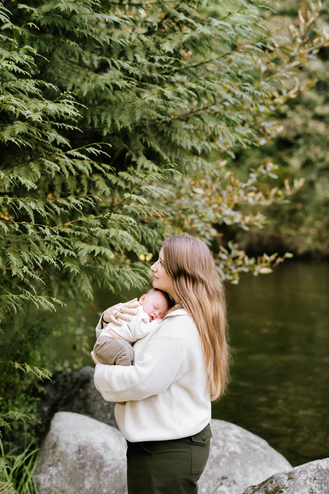 Mother cradling her newborn on rocks beside a river