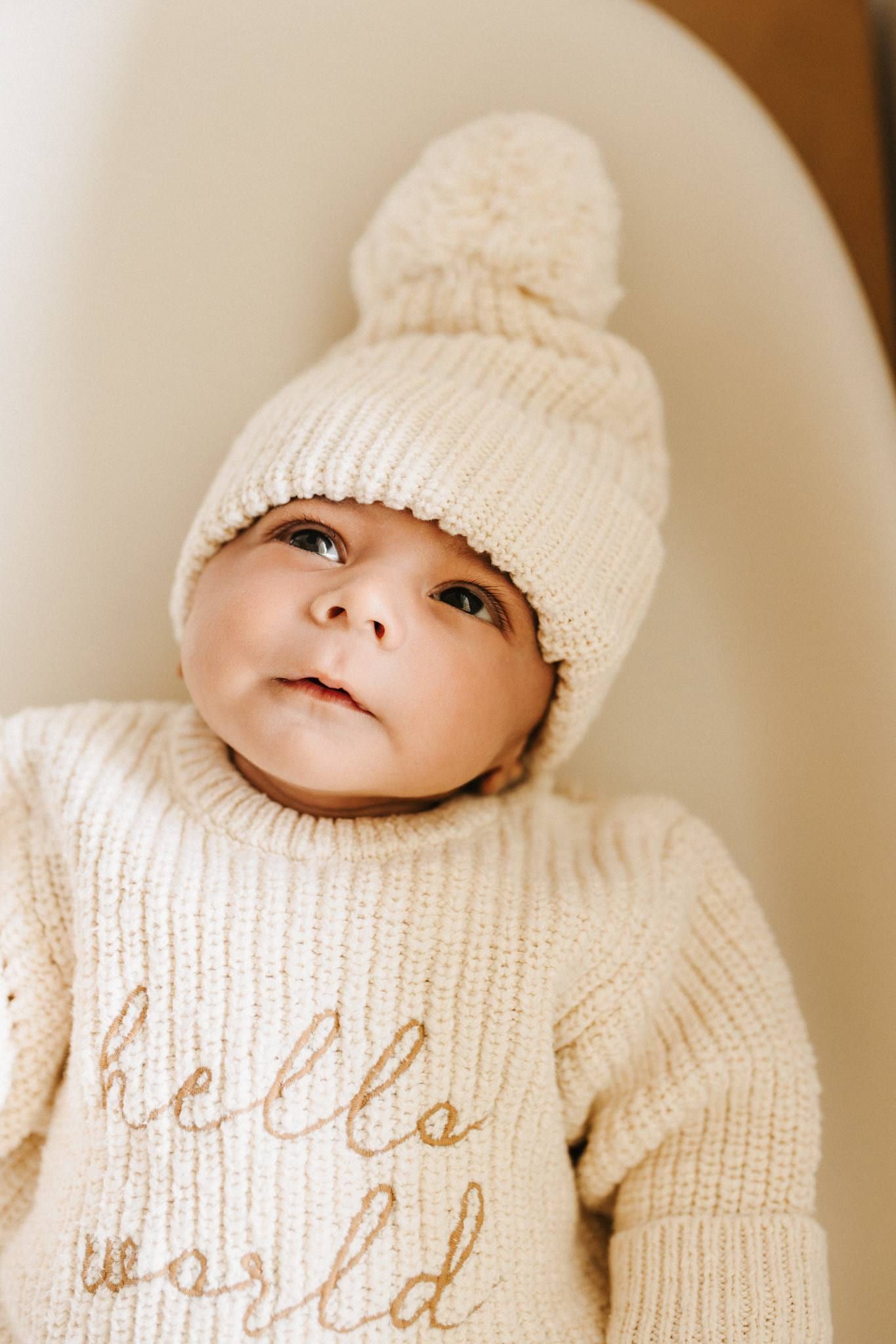 Newborn in a knitted bobble hat and "hello world" sweater