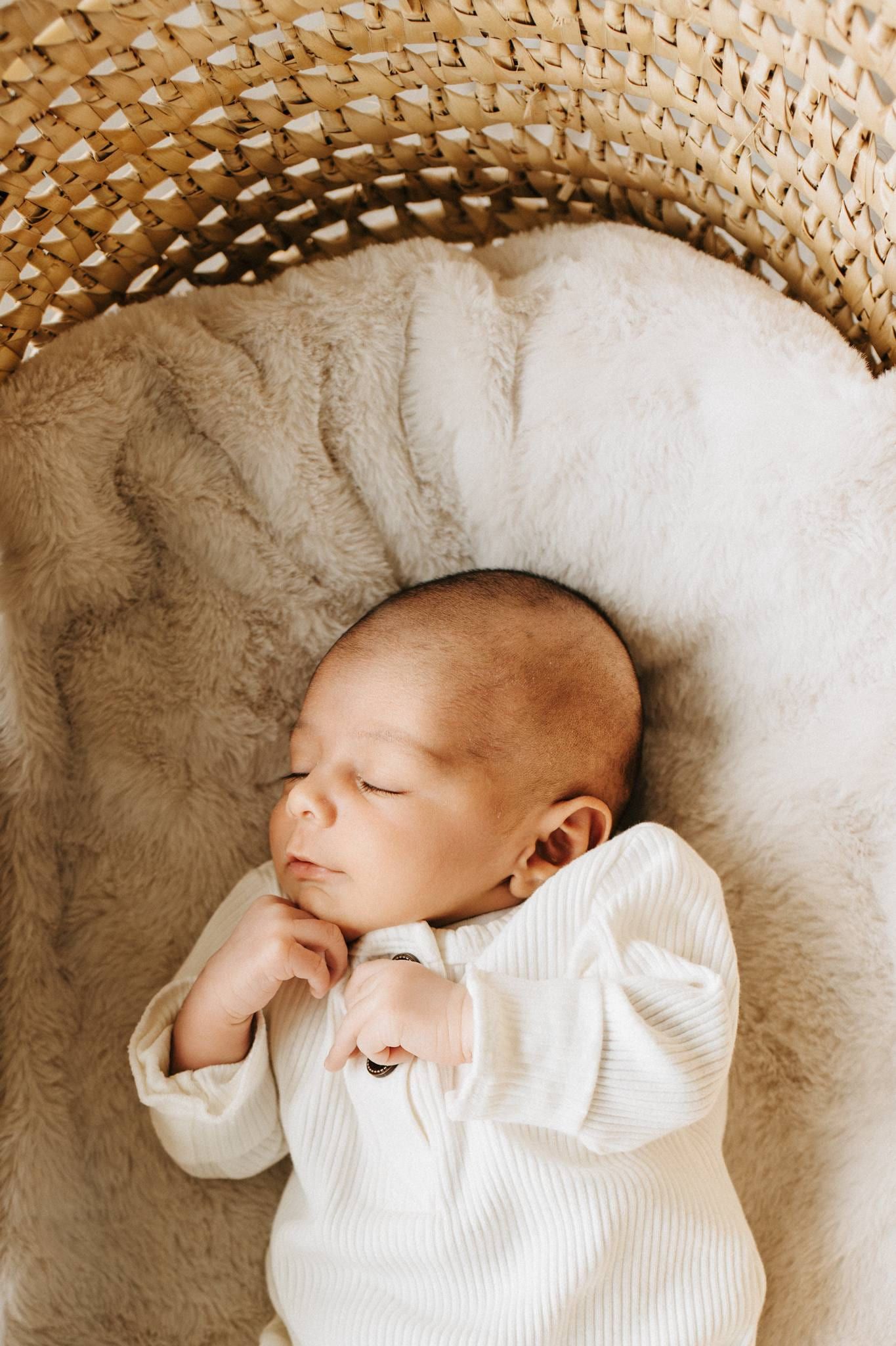Sleeping newborn in a white romper in a woven basket
