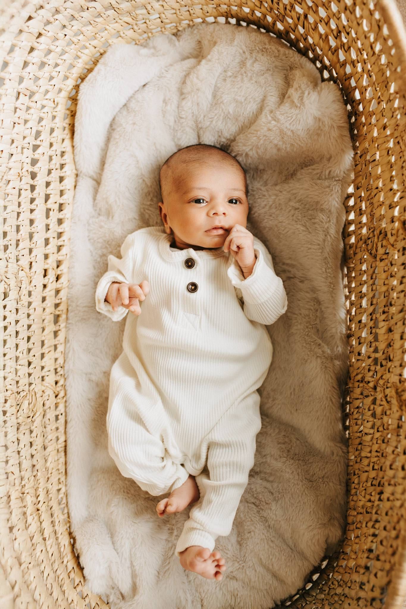 Newborn in a cream romper lying in a woven Moses basket