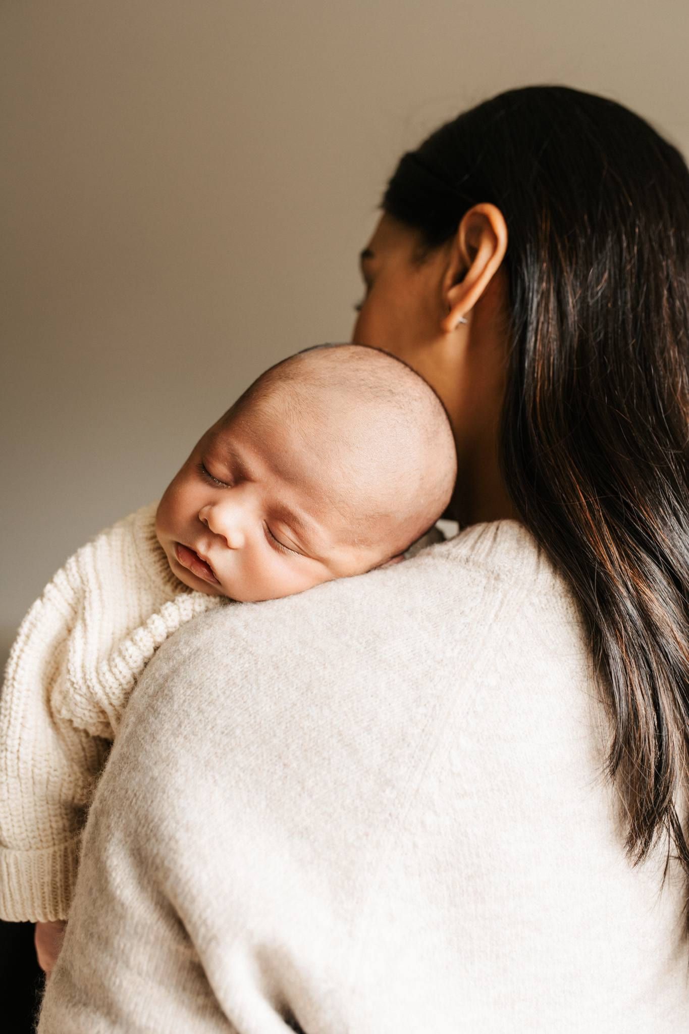 Newborn asleep on a mother's shoulder in a cream sweater