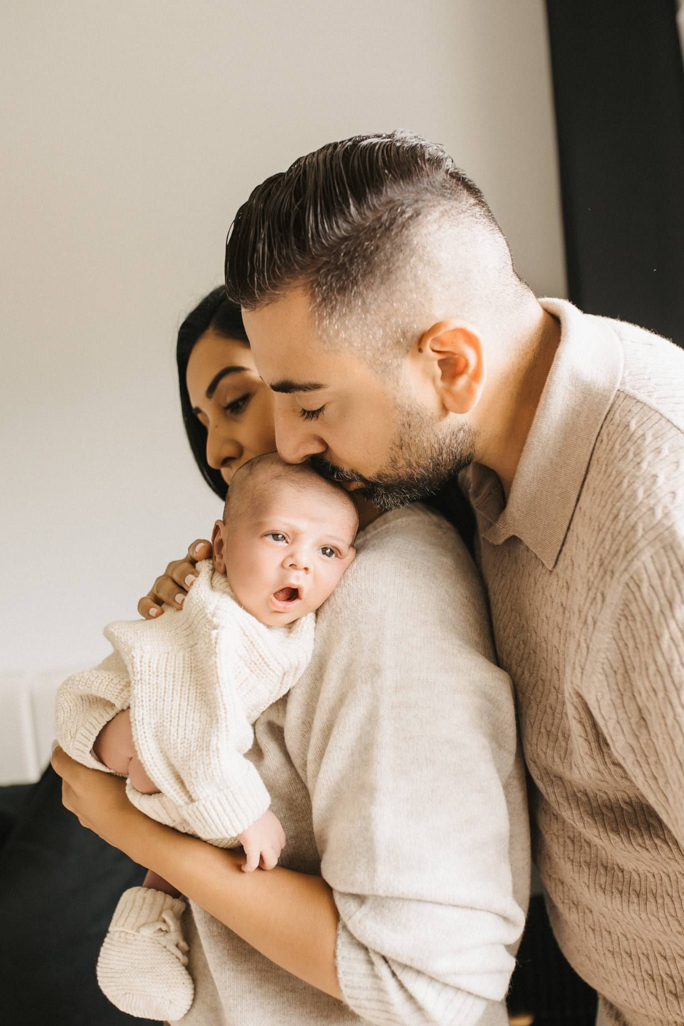 Parents kissing their newborn cradled in the father's arms