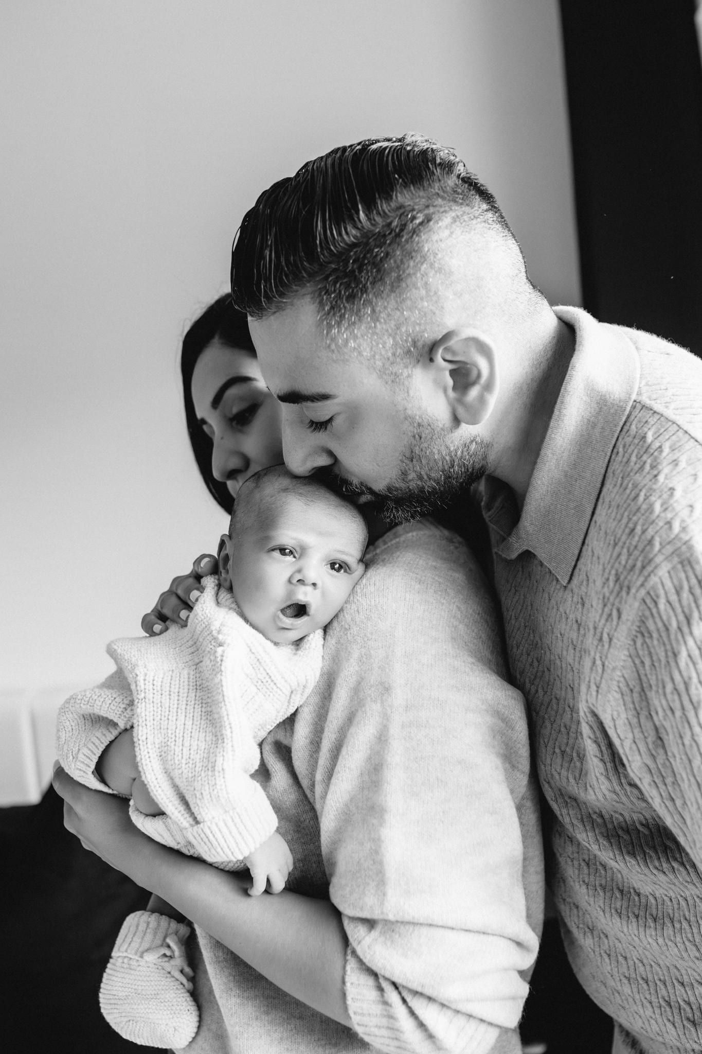 Black-and-white photo of parents kissing their newborn's cheeks