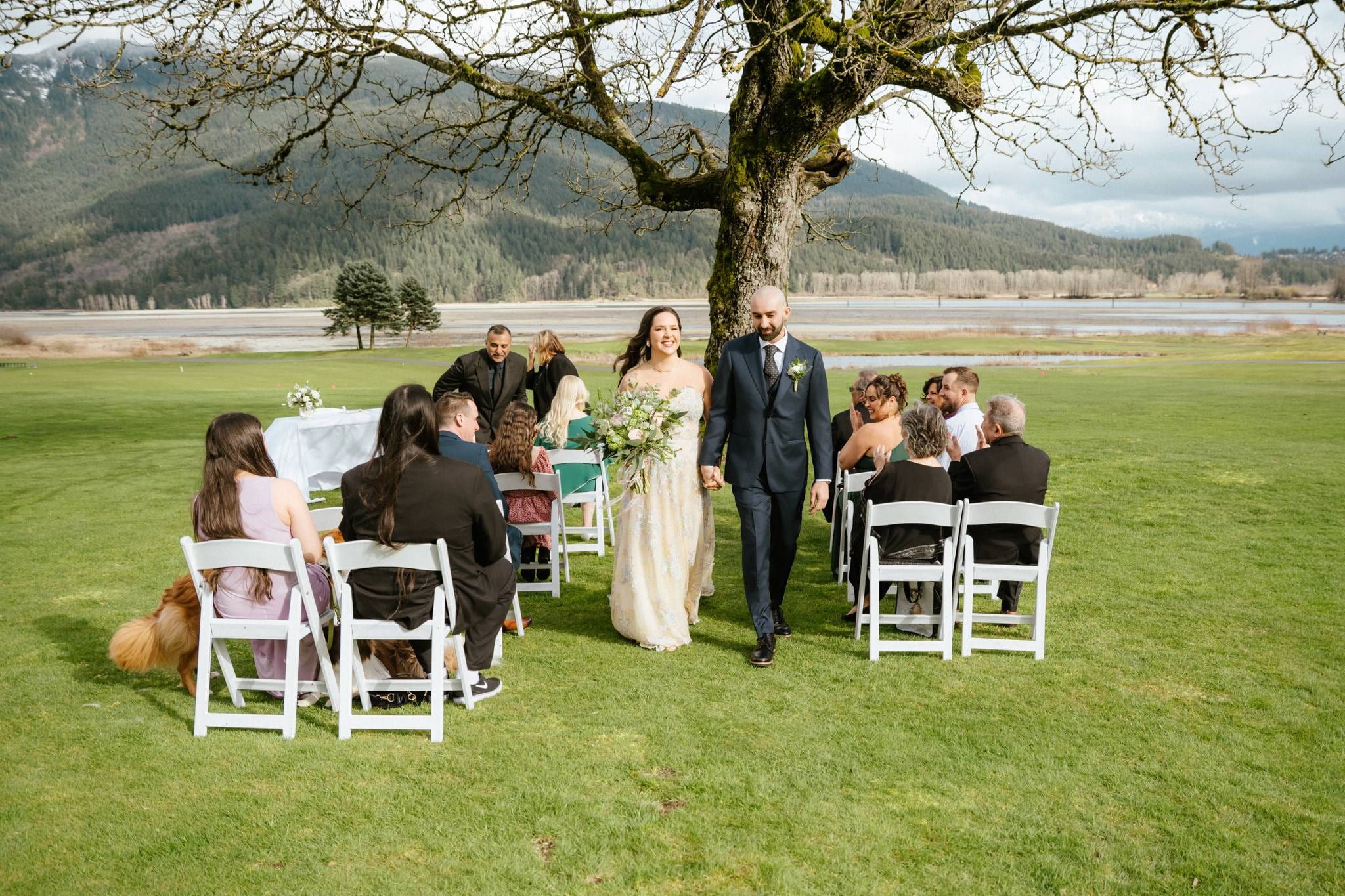 Andrea and Dusten walking back down the aisle between their guests beneath a bare oak