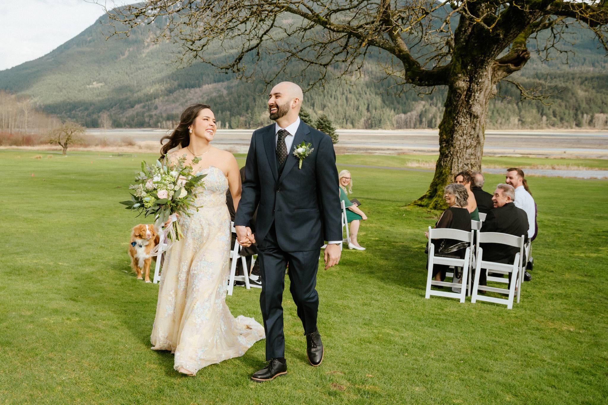 Newlyweds walking back down the aisle past their guests under a bare oak tree
