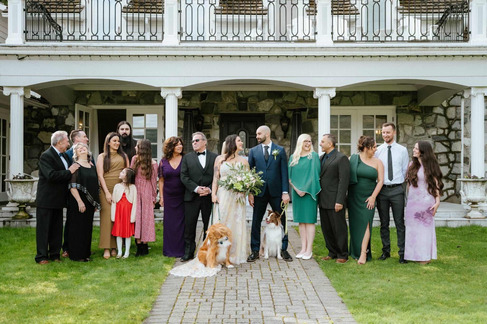 Wedding party and family posed on the steps of a stone lodge with two dogs