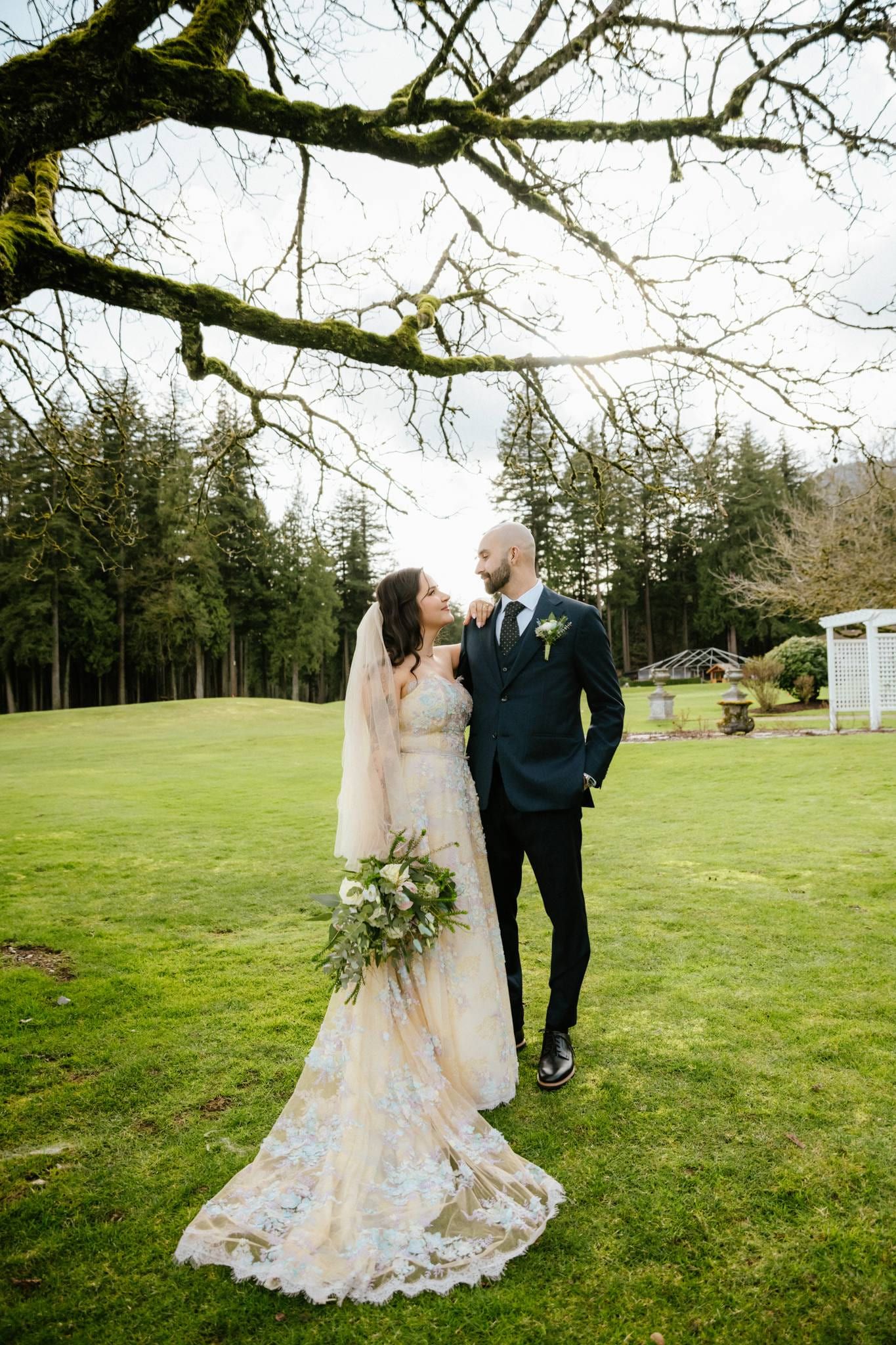 Bride and groom under an oak tree, her train spread on the grass