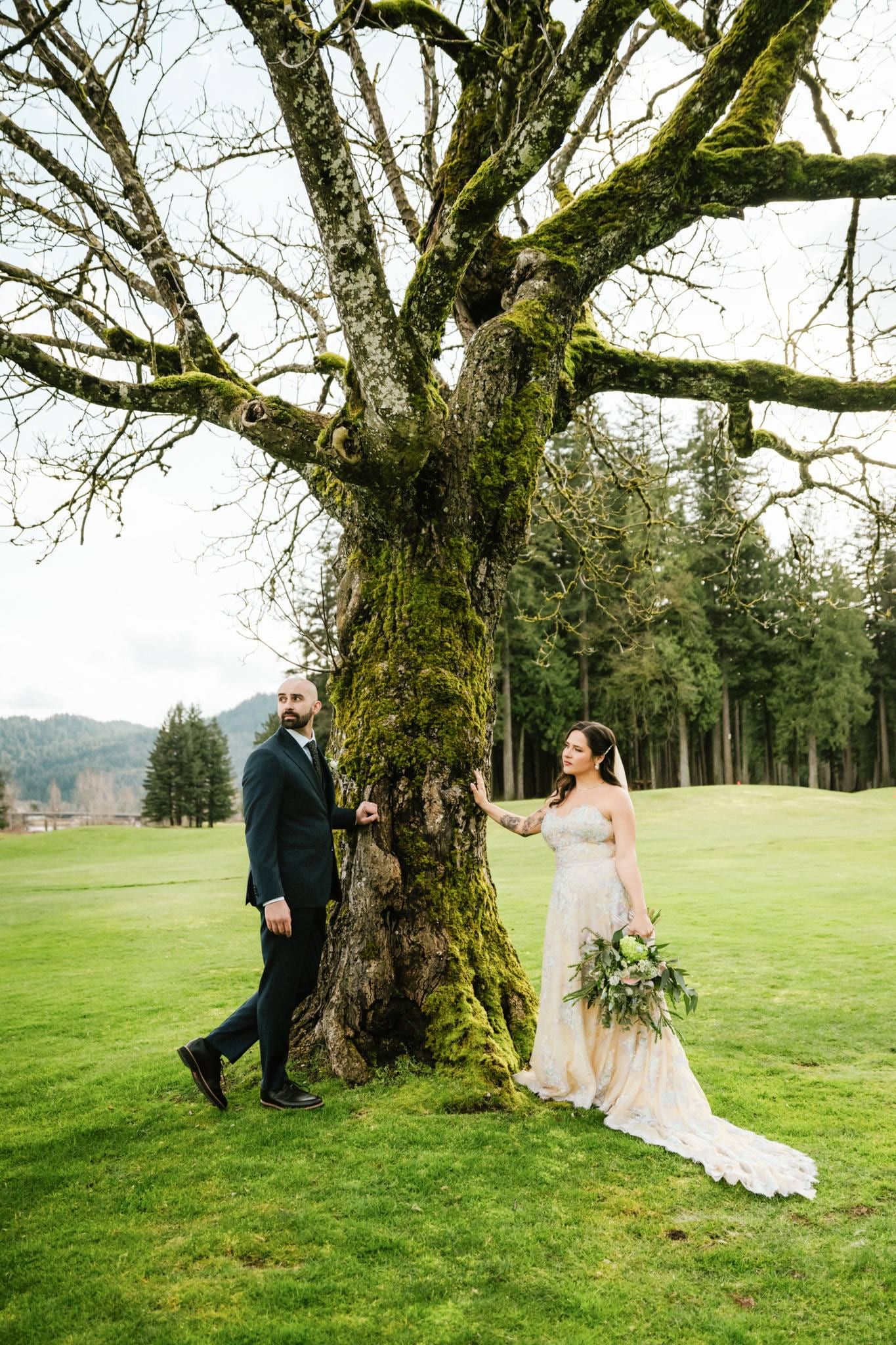 Couple holding hands around a mossy tree trunk on the golf-course lawn