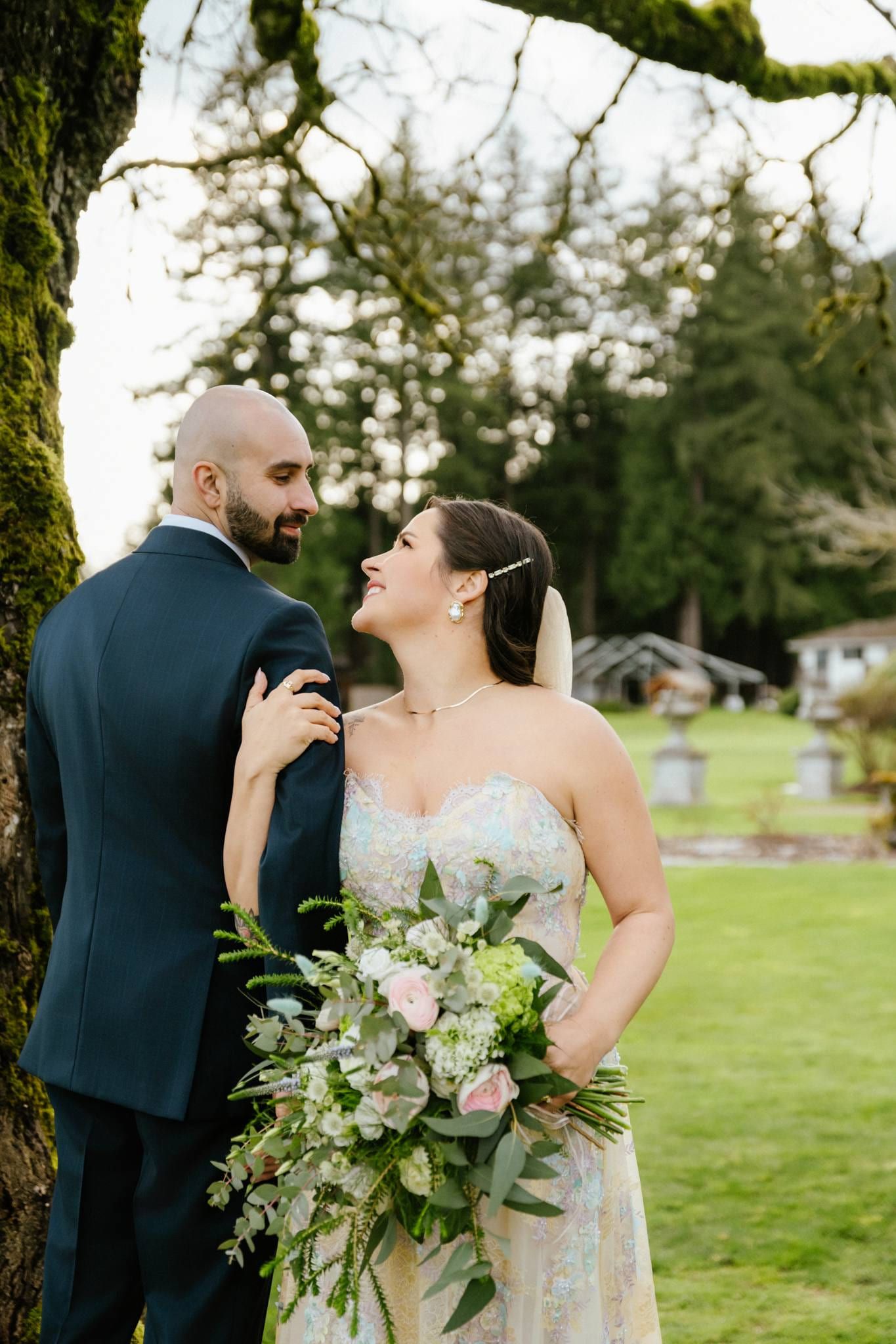 Groom kissing the bride's temple as she holds her bouquet on the lawn