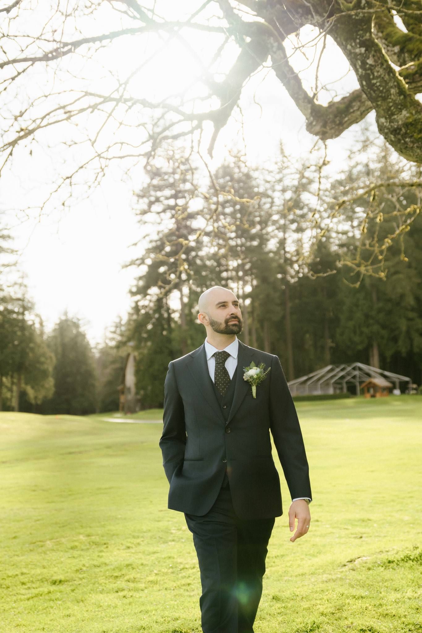 Groom in a navy suit standing on the lawn with his hands in his pockets