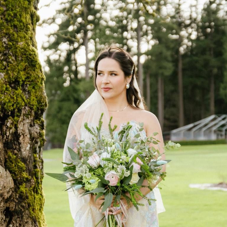 Andrea holding her bouquet beside a mossy tree on her wedding day