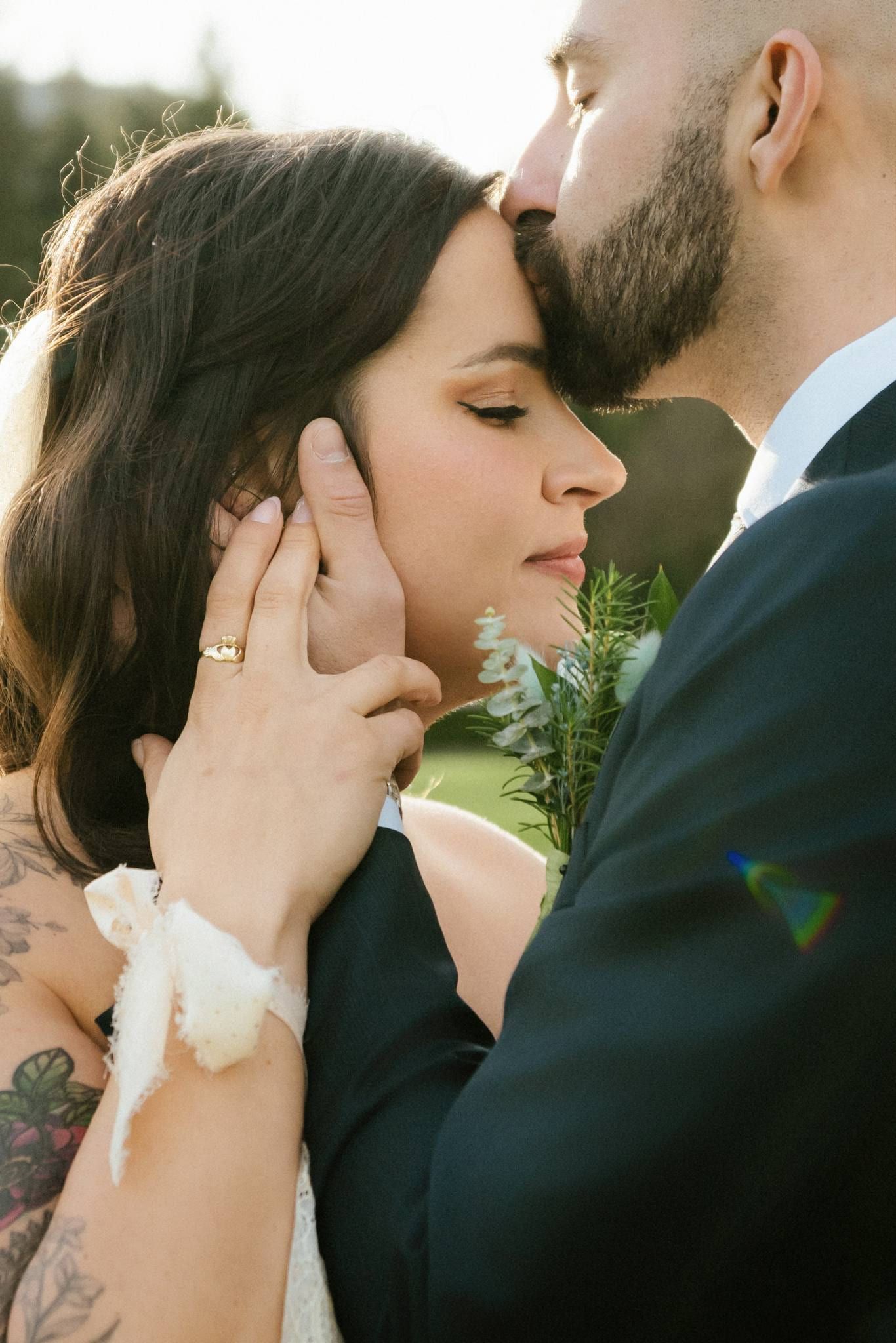 Groom kissing the bride's forehead, her hand at his cheek