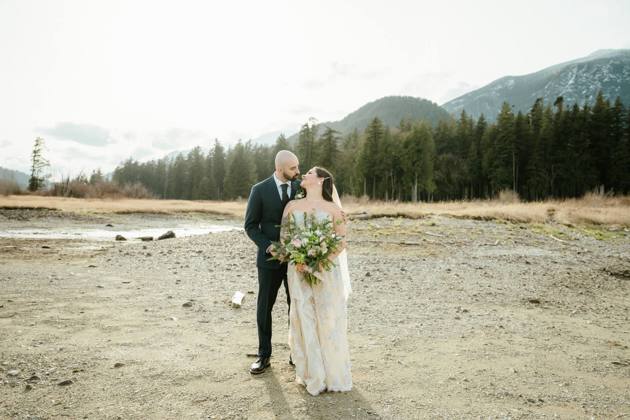 Couple standing together on the wide riverbed with mountains in the distance