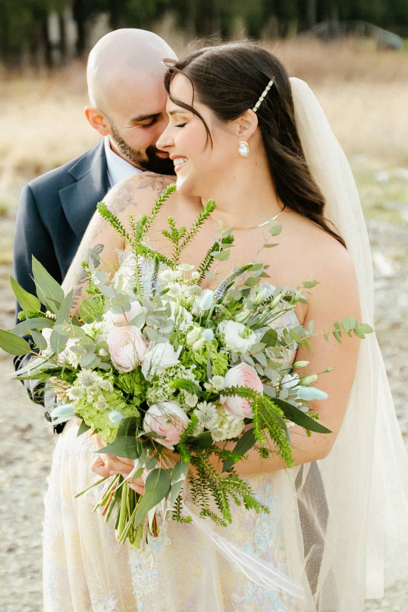 Groom kissing the bride's forehead as she holds a pastel bouquet
