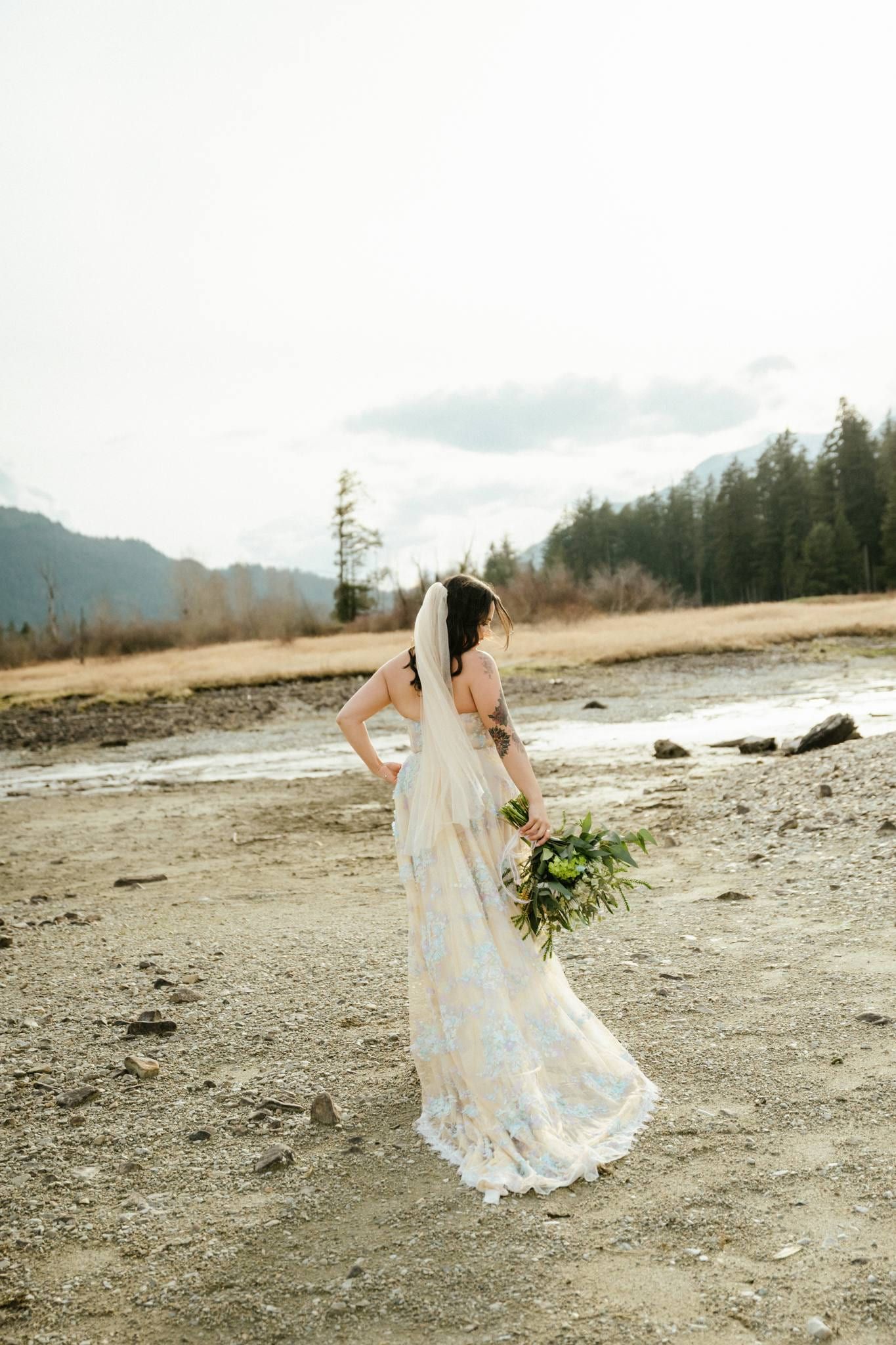 Bride in a lace gown standing alone on the riverbed