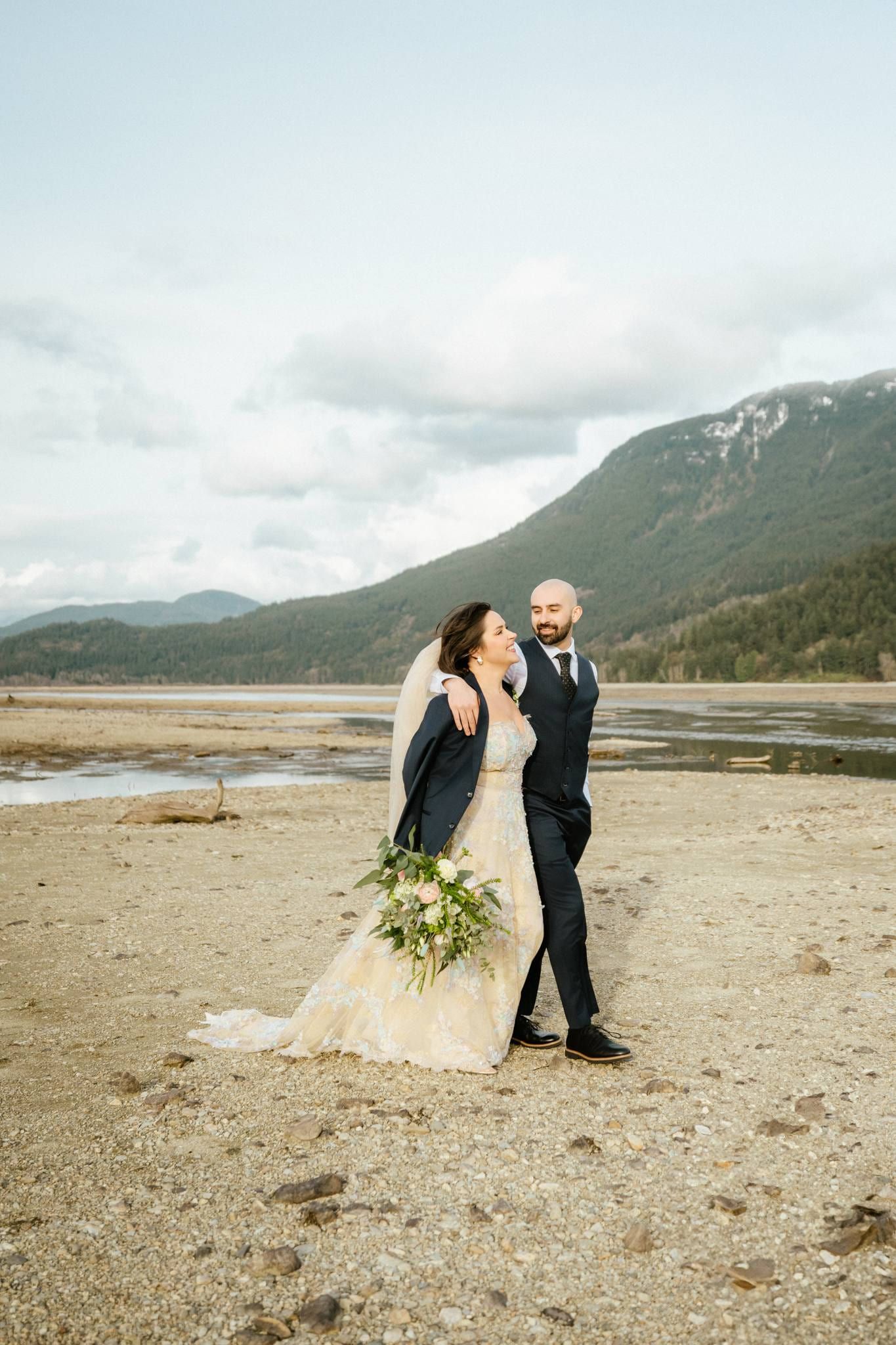 Bride and groom embracing on the riverbed under a moody sky
