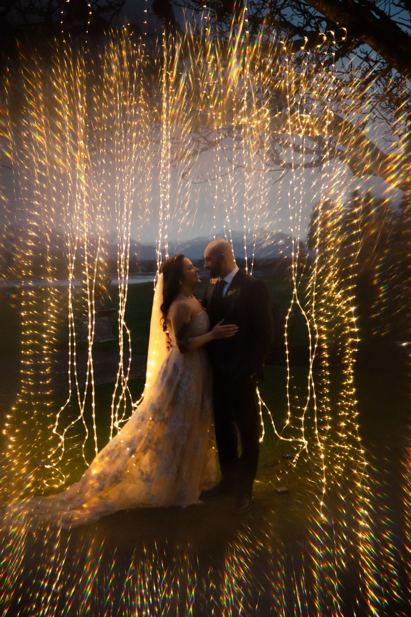 Couple kissing beneath strands of fairy lights at night