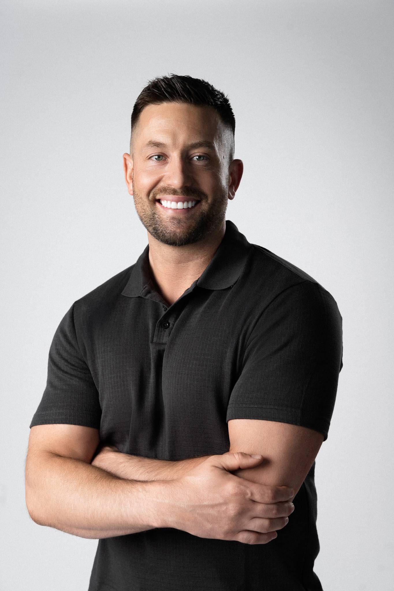 Man in a black polo with arms crossed, smiling