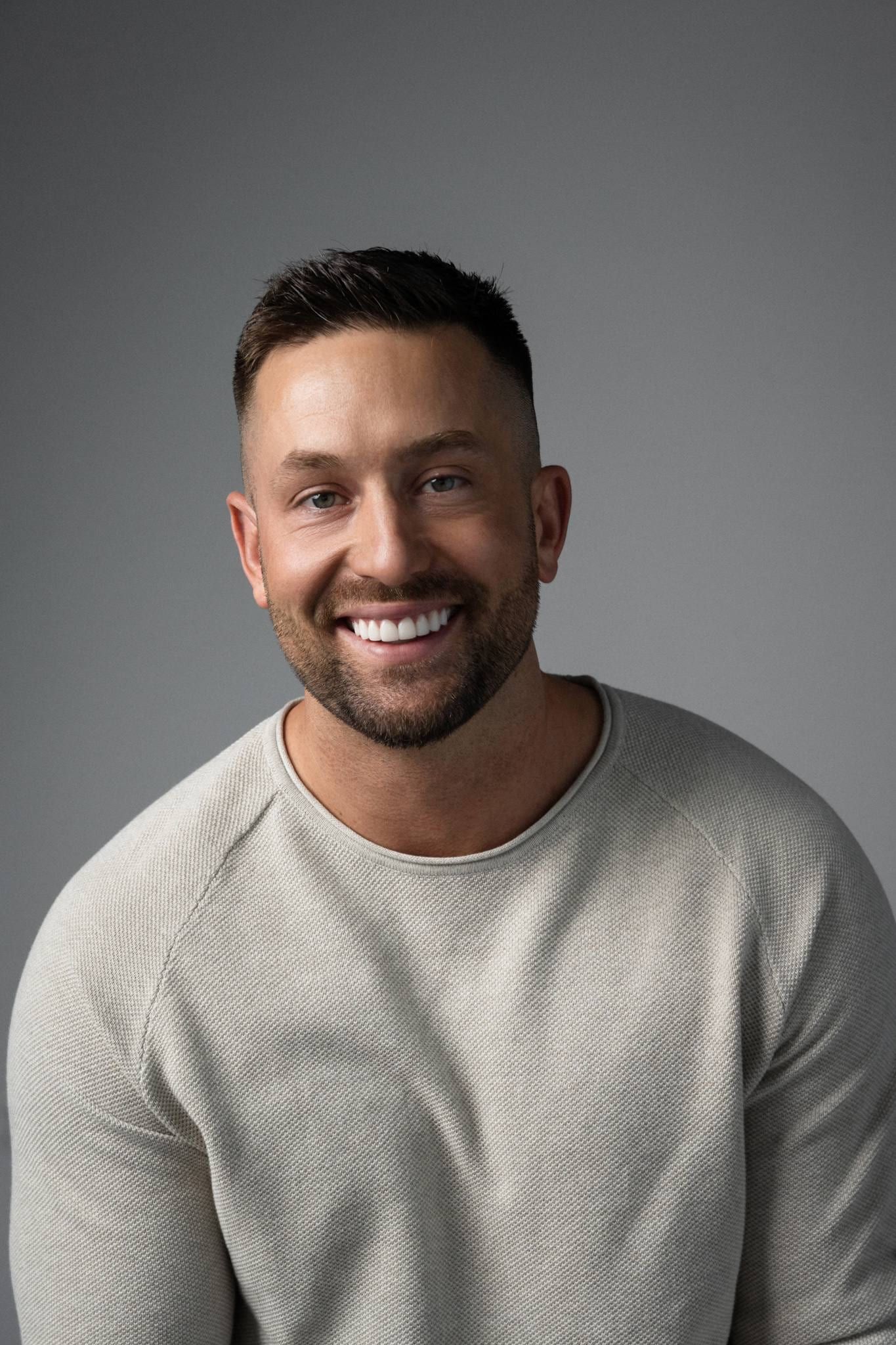 Smiling man in a cream sweater on a grey backdrop