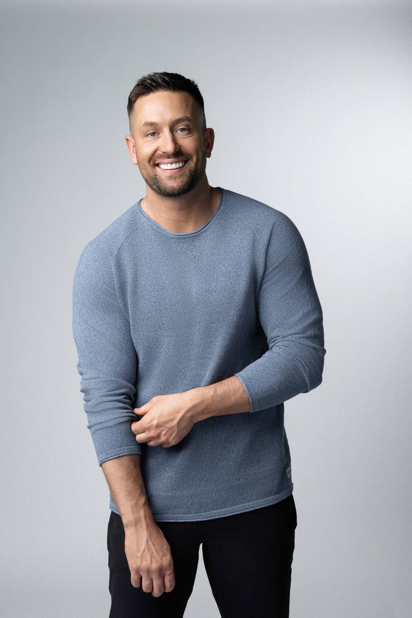 Smiling man in a blue sweater on a grey studio backdrop