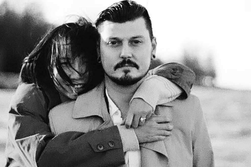 Couples photos on the beach, black-and-white photo of a woman hugging a man from behind on a windswept beach, her hair blowing across her face