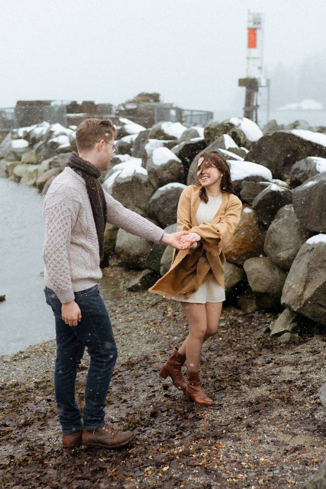 Winter engagement shoot, couple dancing hand in hand on a rocky beach in winter