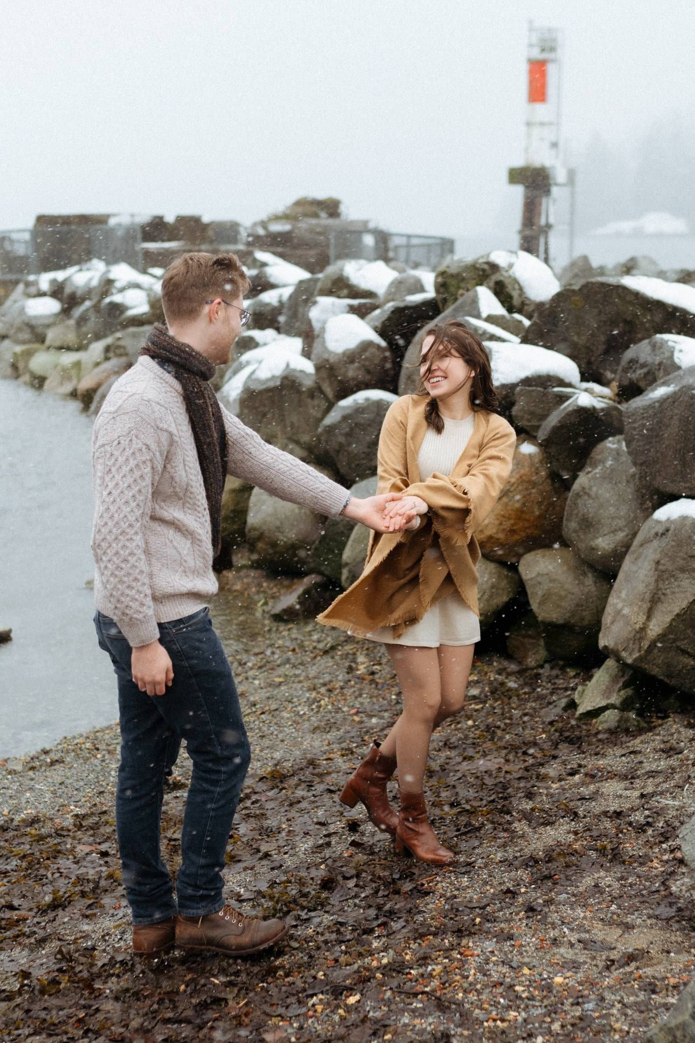 Engagement pictures in winter, couple dancing hand in hand on a rocky beach in winter