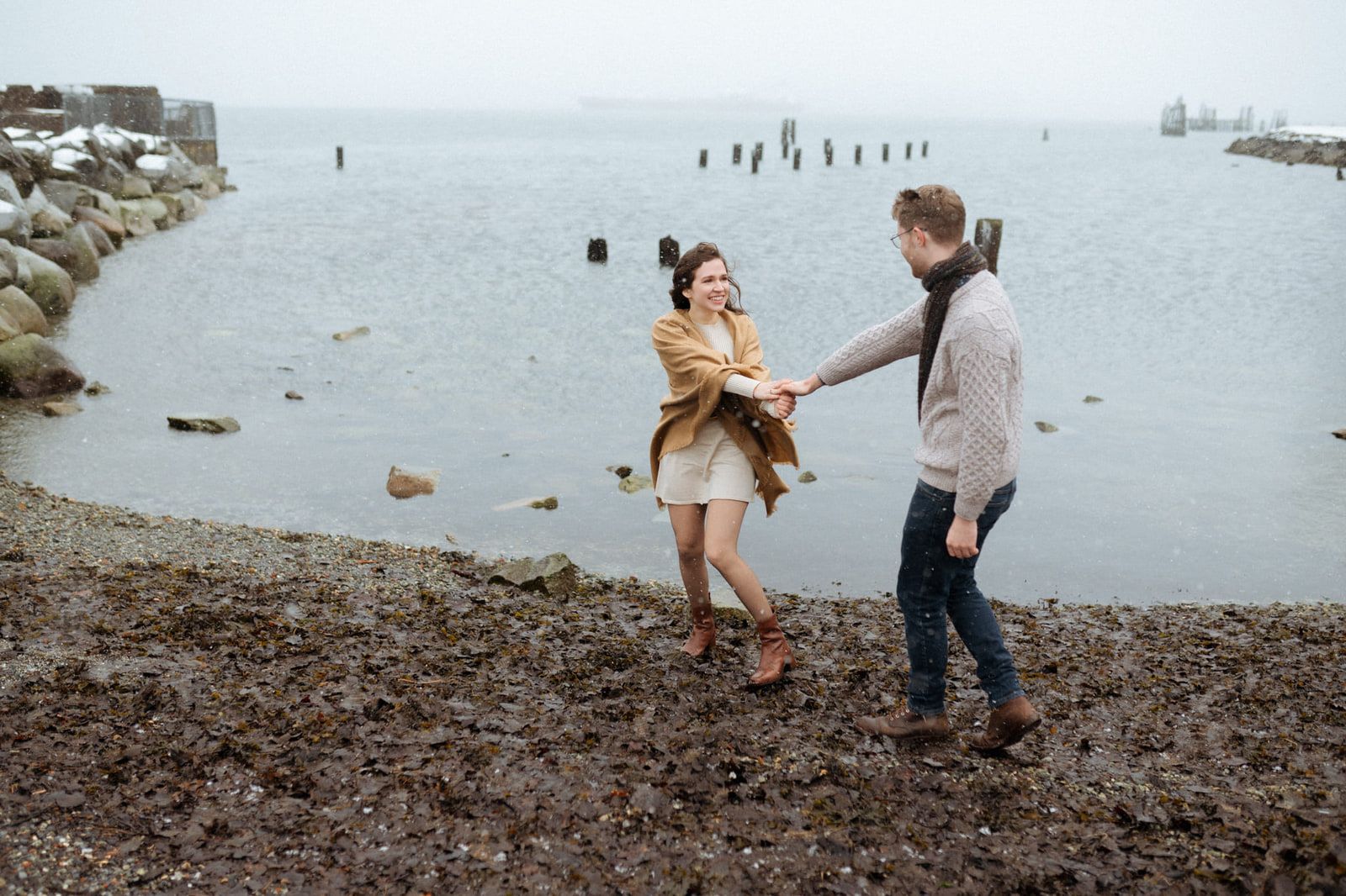 Beach engagement pics, couple dancing hand in hand on a misty pebble beach