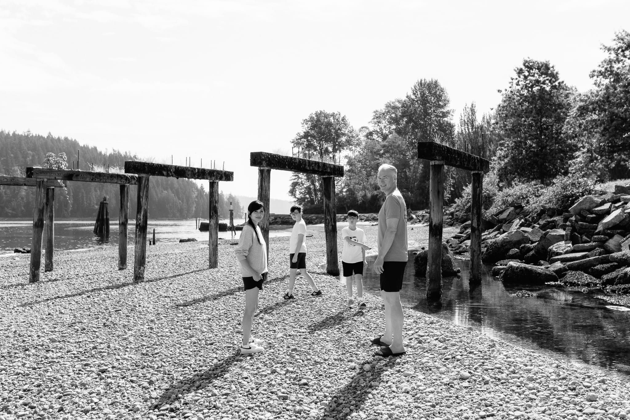 Family black and white photo on a pebble beach, a family walking among old pier posts
