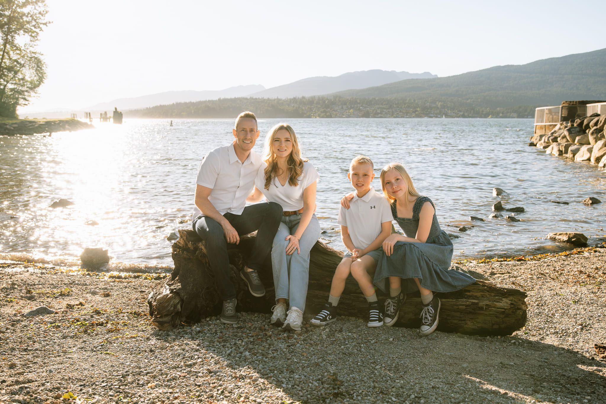 Summer family pictures on the beach by the lake, family of four sitting on a log