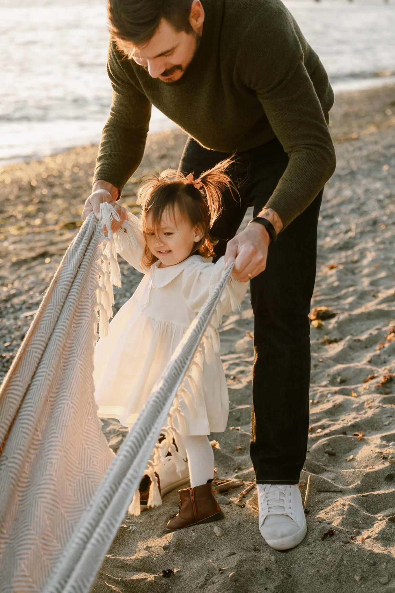 Langley family photos, dad pulling his toddler daughter along the sand on a blanket