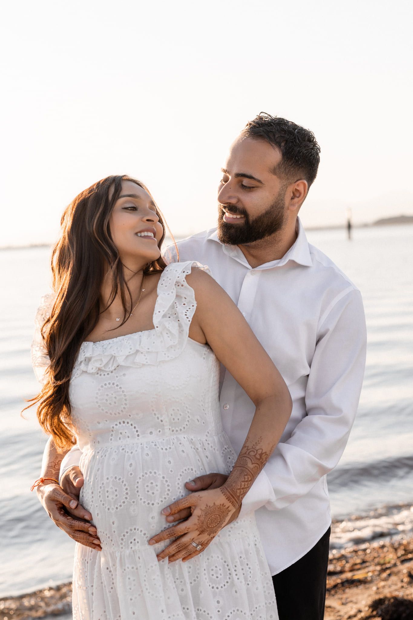 Beach sunset maternity photos, expecting couple smiling at each other