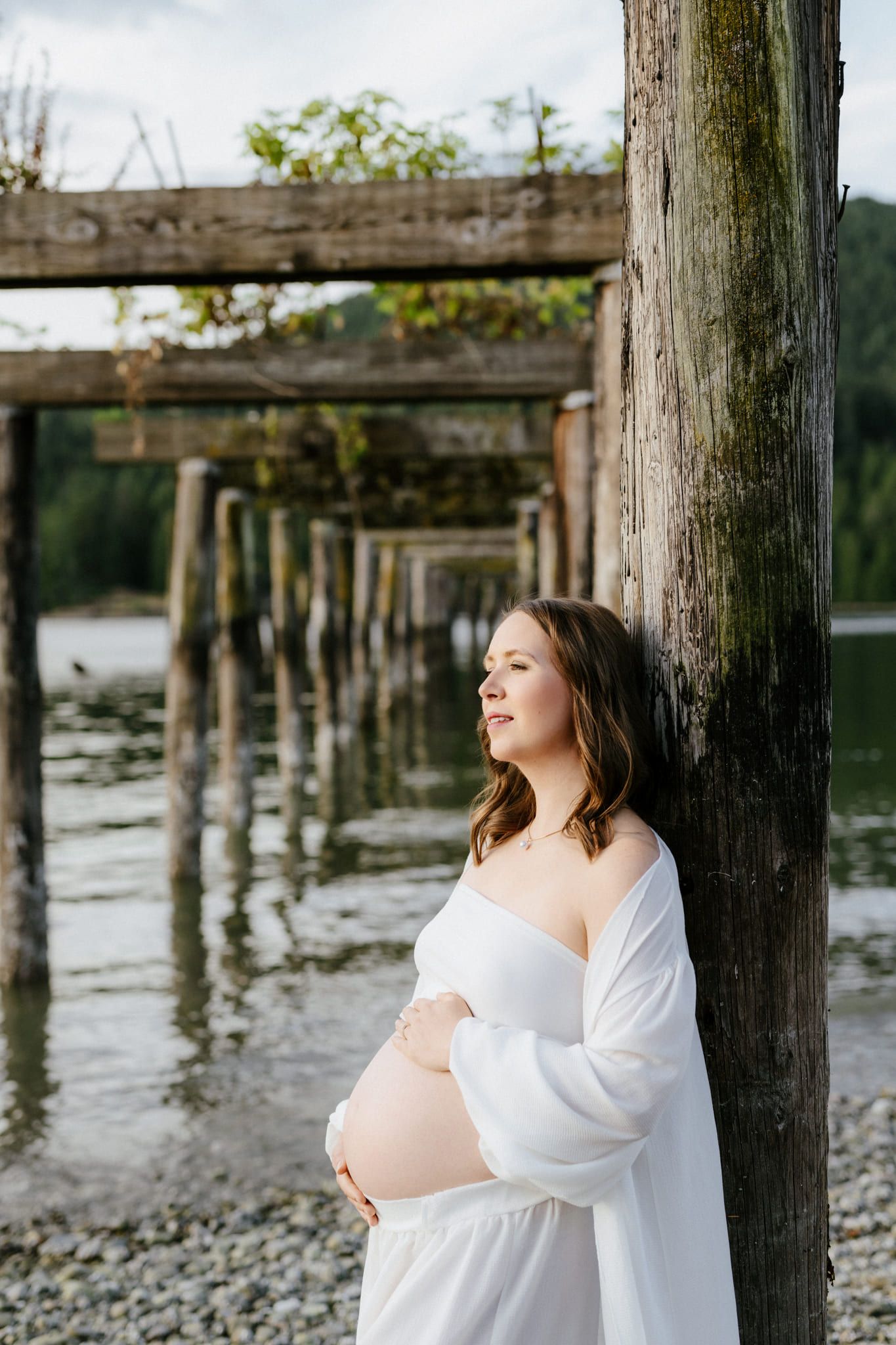 Maternity beach photoshoot, mom-to-be leaning on a wooden pier post
