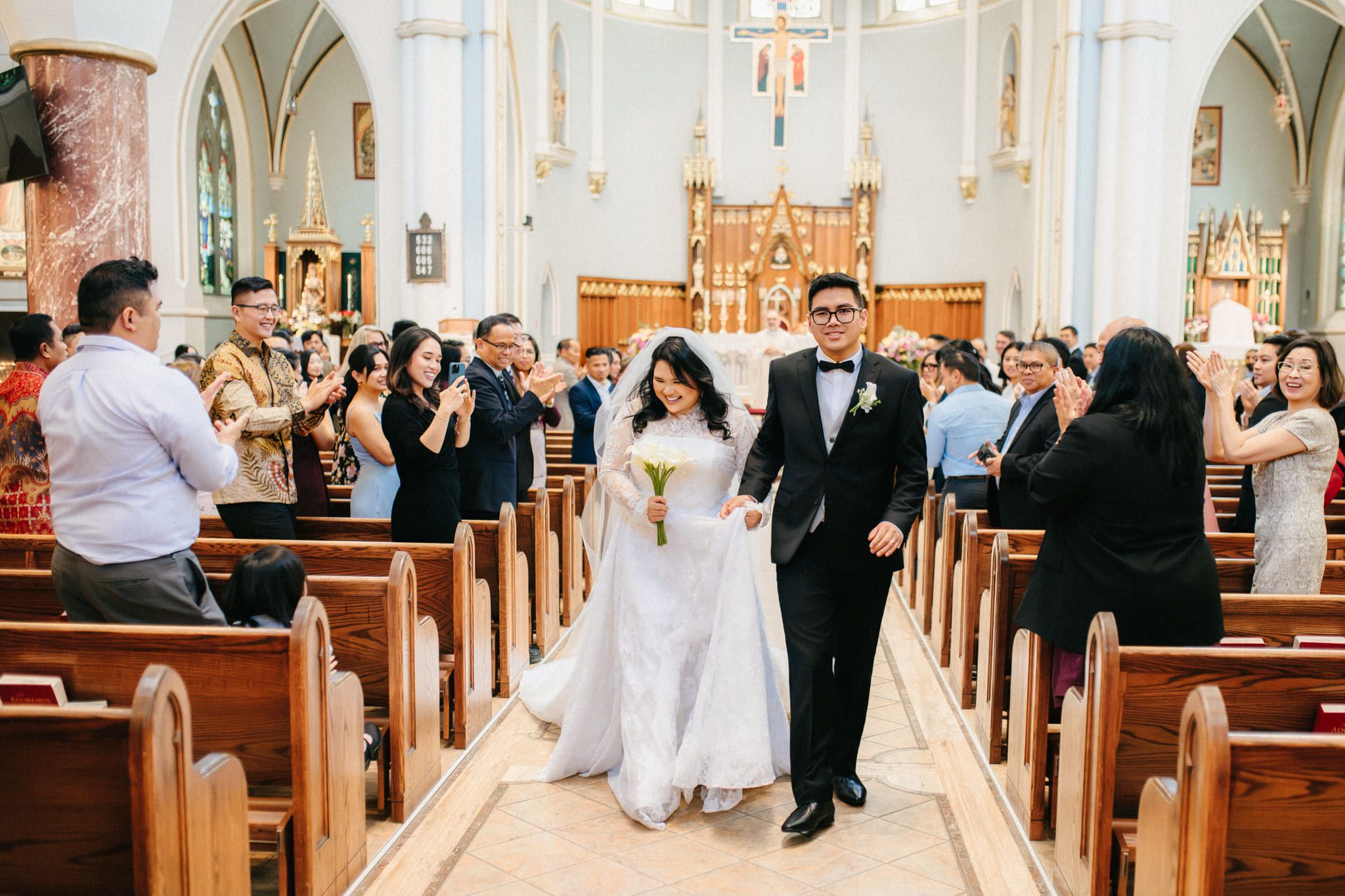 Bridal shoot, bride and groom walking down the aisle of a church as guests cheer