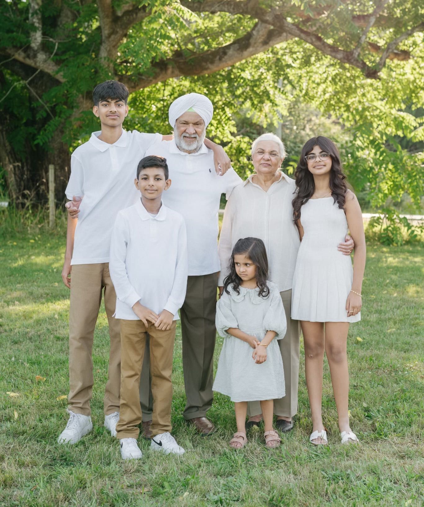 Grandparents and their four grandchildren dressed in white beneath a large tree