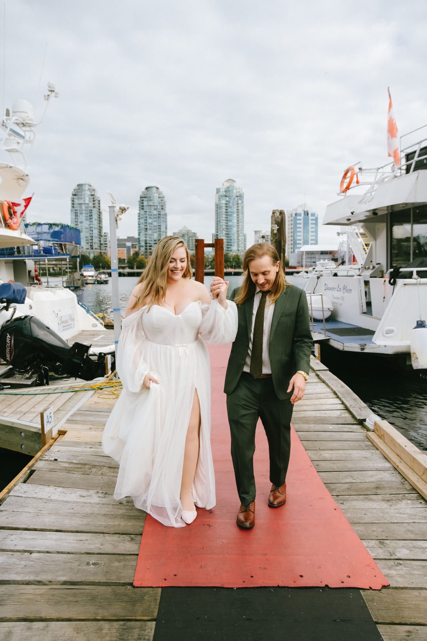 Outdoor bridal photoshoot, bride and groom walking along a dock past moored boats