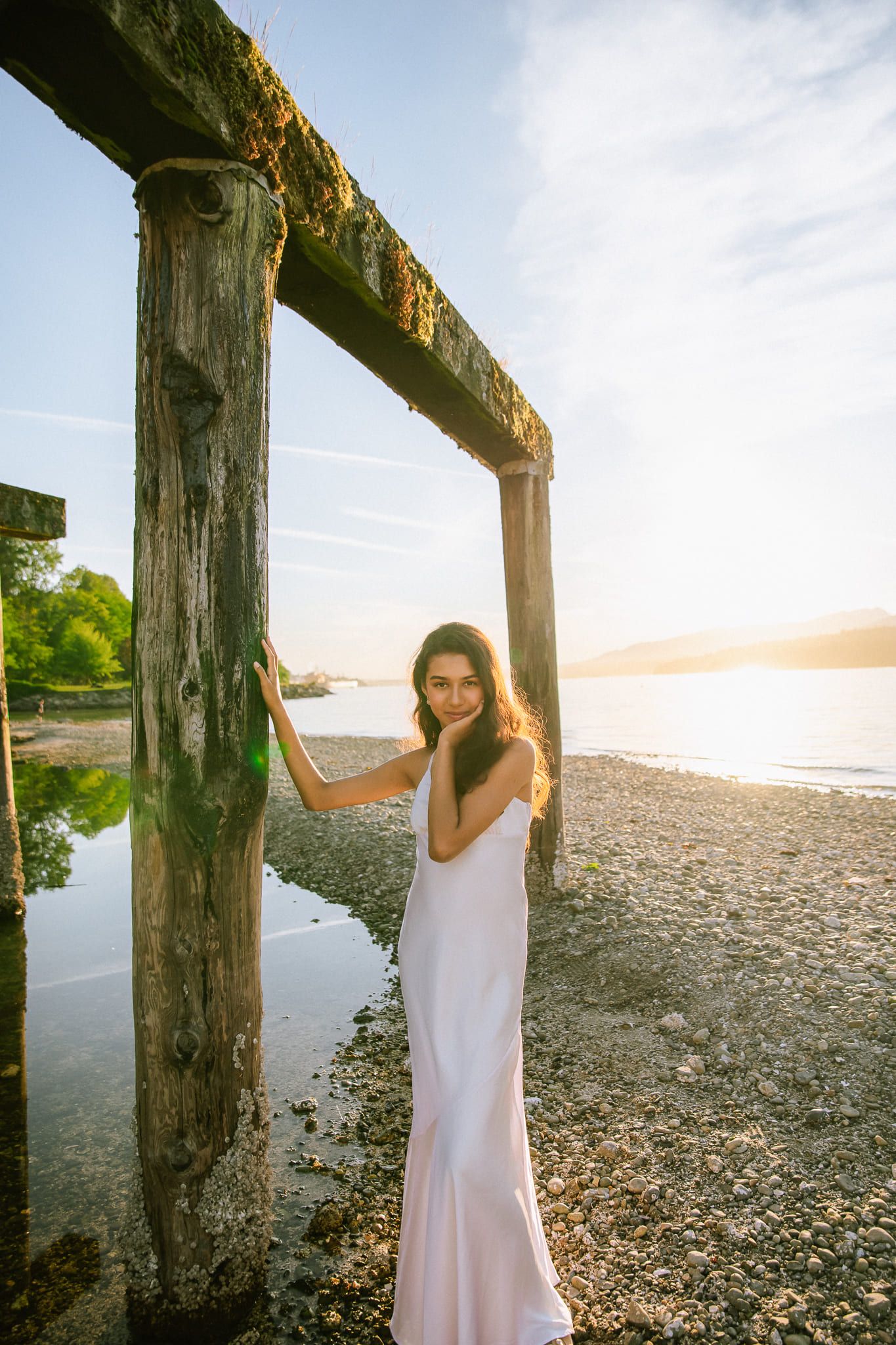 Sunset portrait photography, woman in a slip dress leaning on a wooden pier post