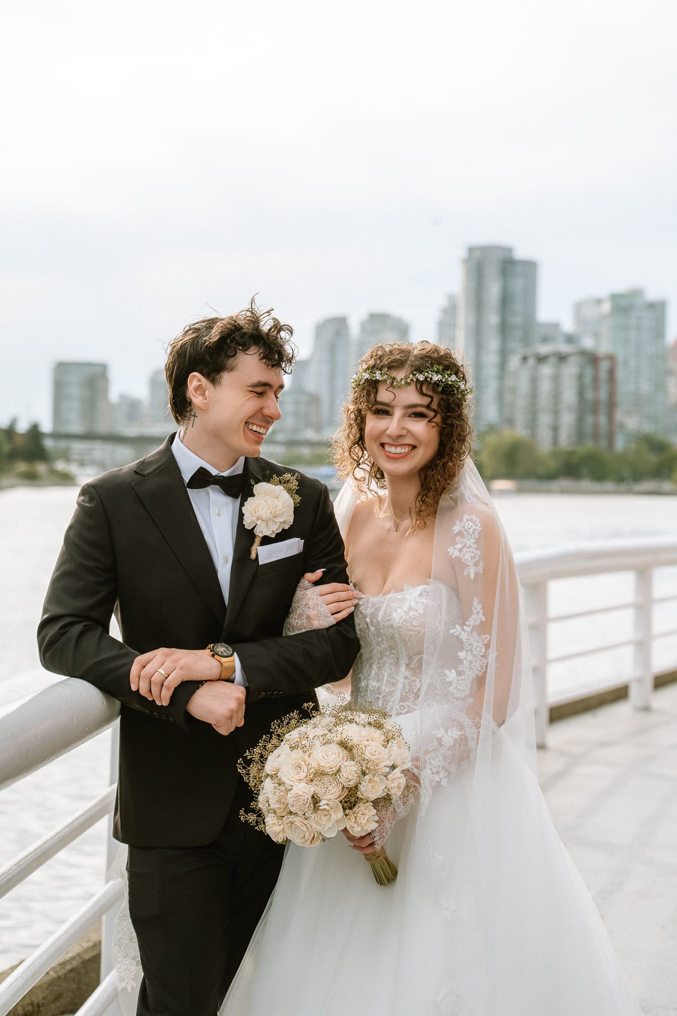 Bride photoshoot, bride and groom arm in arm by the water with the city skyline behind