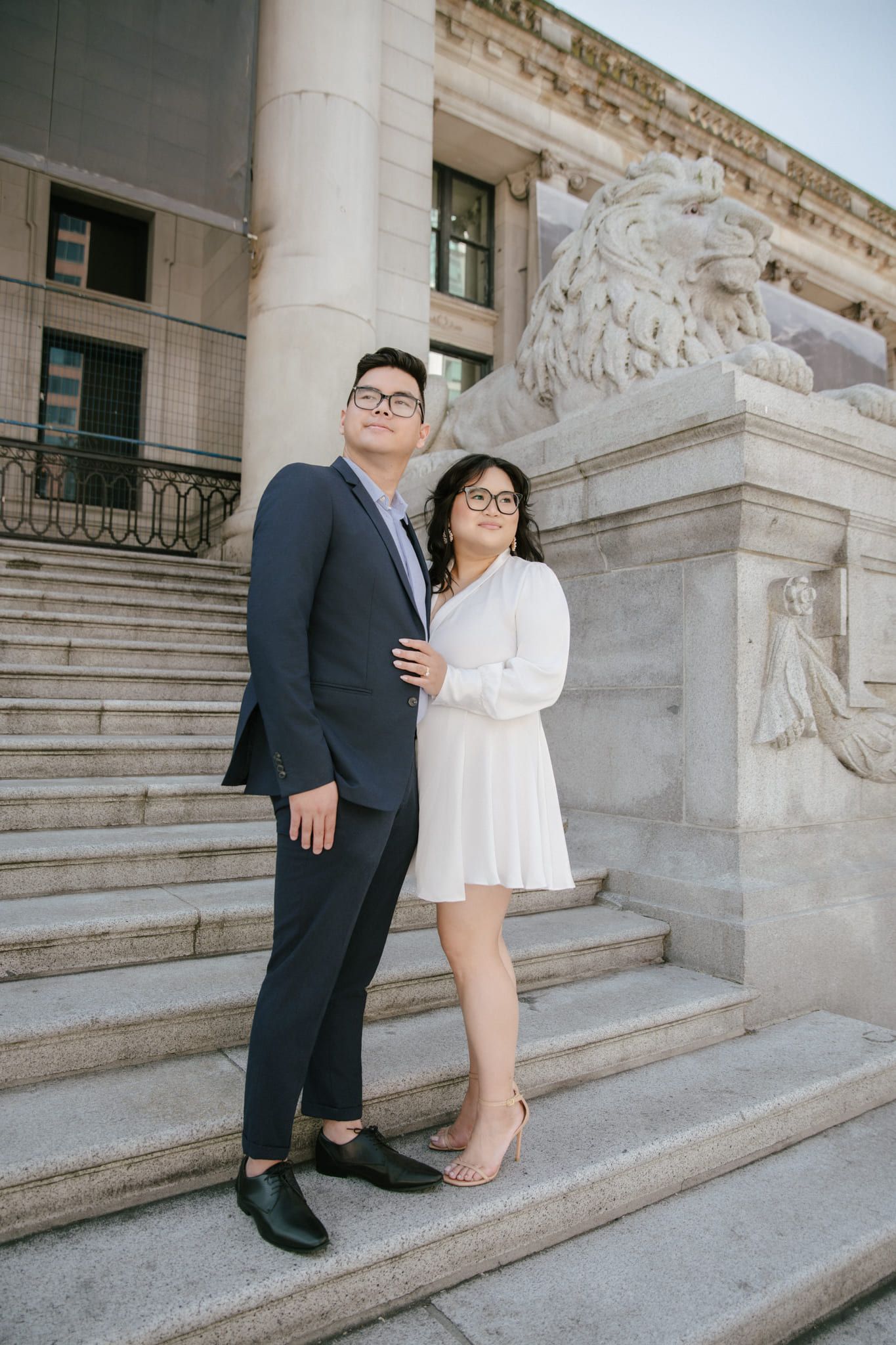 Creative wedding photography, a couple in a navy suit and a short white dress on the stone steps of a grand building beside a carved lion