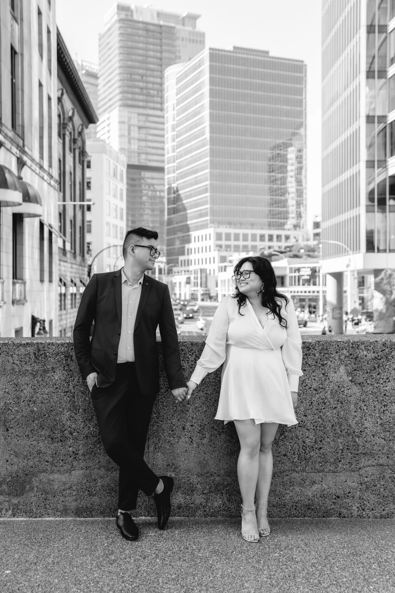 Natural wedding photography against a wall among downtown towers, black-and-white photo of a couple holding hands