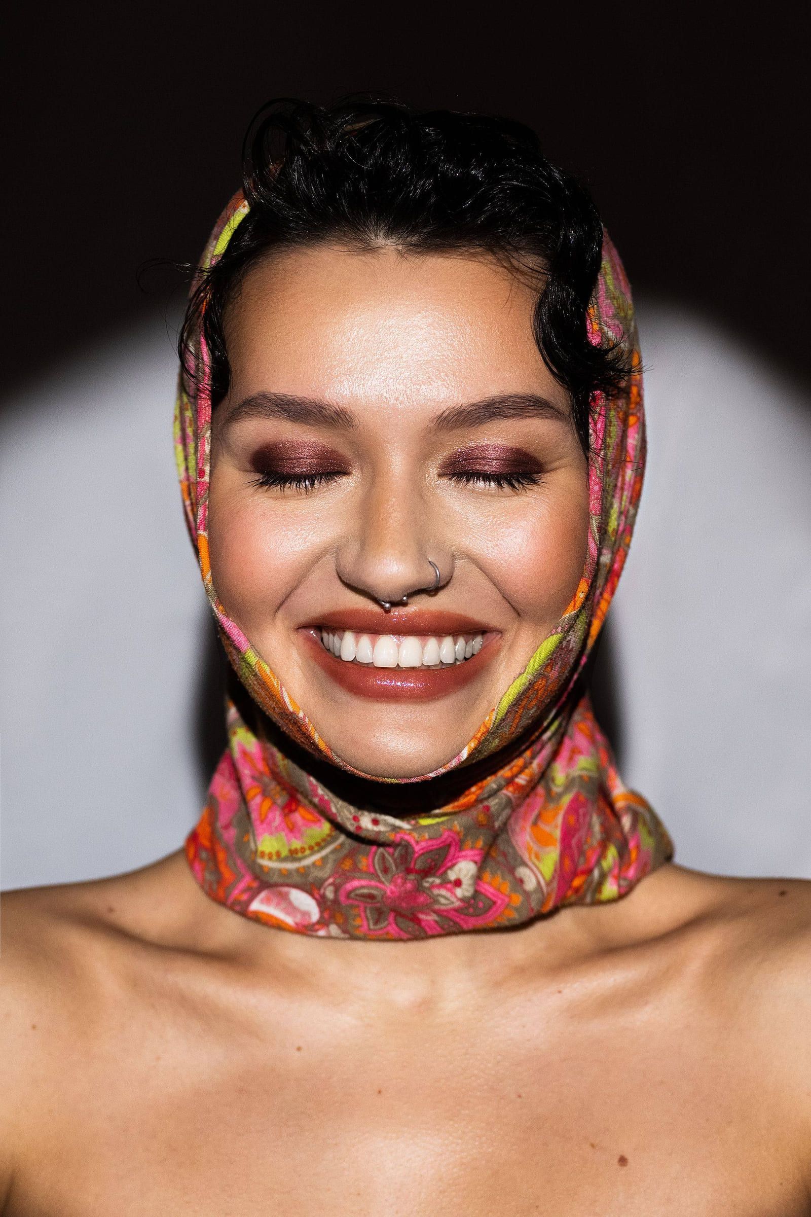 Model laughing in a colourful printed headscarf against a dark backdrop