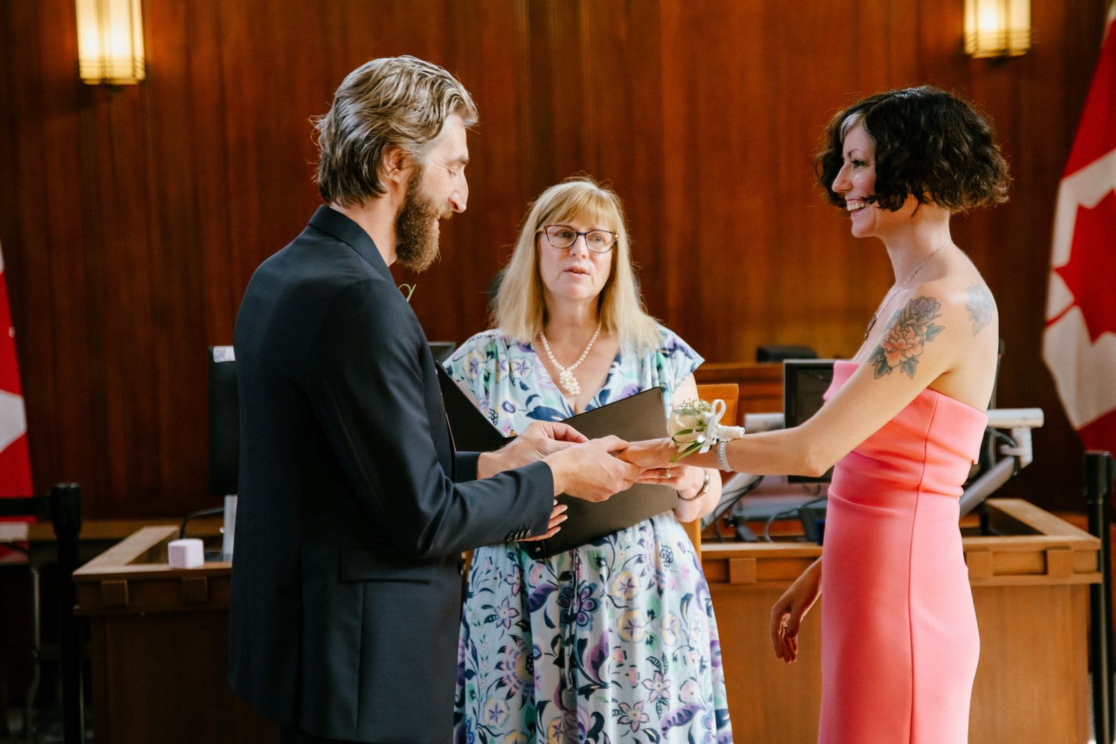 Vancouver elopement photography, a couple exchange rings before an officiant in a wood-panelled registry room, the bride in a coral dress