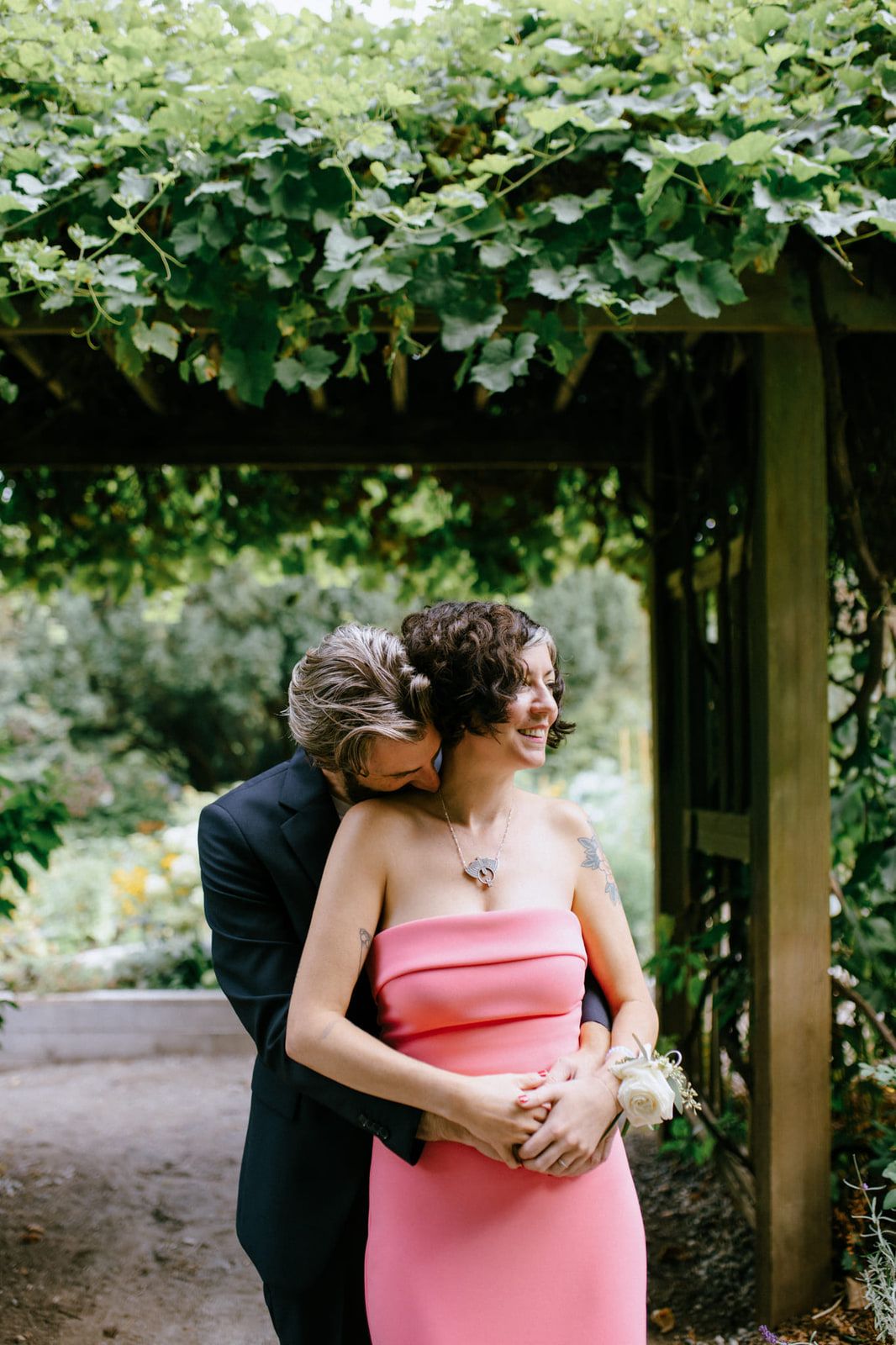 Small wedding photography, couple embracing under a vine-covered pergola